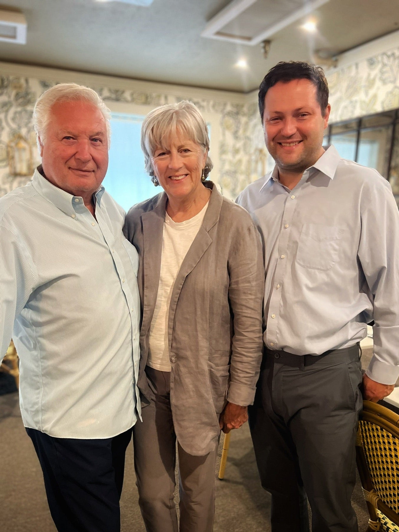 Three people standing together indoors with a decorative wall in the background